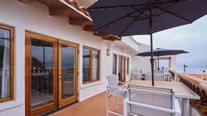 Une terrasse dotée de meubles blancs, de grands parasols et de portes vitrées donnant sur une autre terrasse.