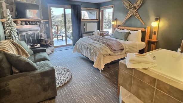 A bedroom with a large bed, a sofa, a fireplace, a TV, and a bathroom with a bathtub. - Slope-Side Pet-Friendly Studio | In-Unit Jet Tub (Lutsen)