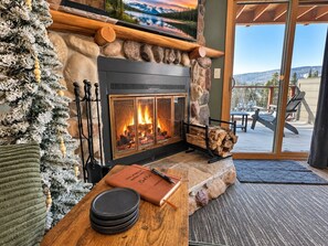 A cozy fireplace with a stone mantle, a Christmas tree, and a view of the outdoors.