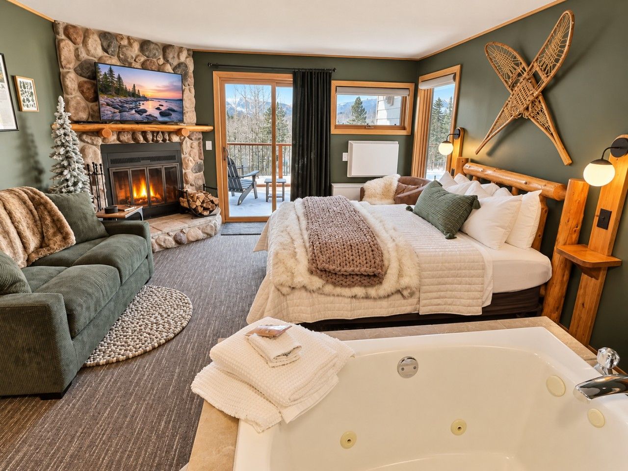 A cozy bedroom with a fireplace, a large bed, a sitting area with a couch, and a view of the outdoors.