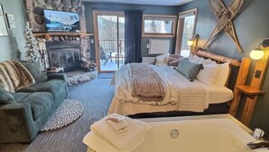 A cozy bedroom with a large bed, a bathtub, a fireplace, and a television. - Slope-Side Pet-Friendly Studio | In-Unit Jet Tub (Lutsen)