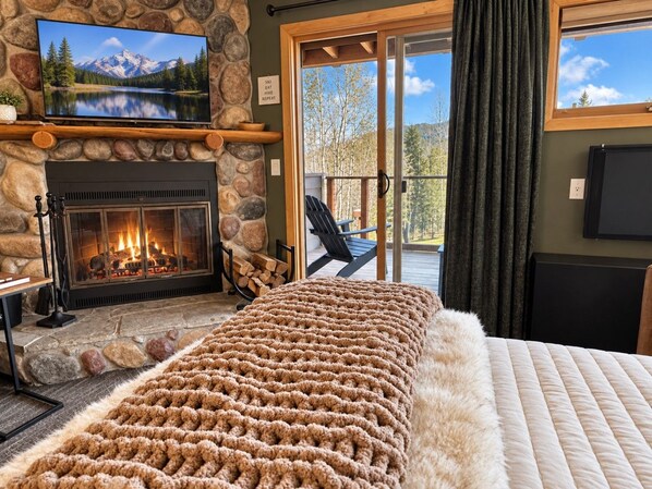 A cozy room with a fireplace, a large bed, and a view of the outdoors. - Slope-Side Pet-Friendly Studio | In-Unit Jet Tub (Lutsen)