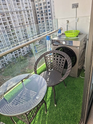 Ein Balkon mit Waschmaschine, einem grünen Korb und zwei Korbstühlen auf Kunstgriffl.