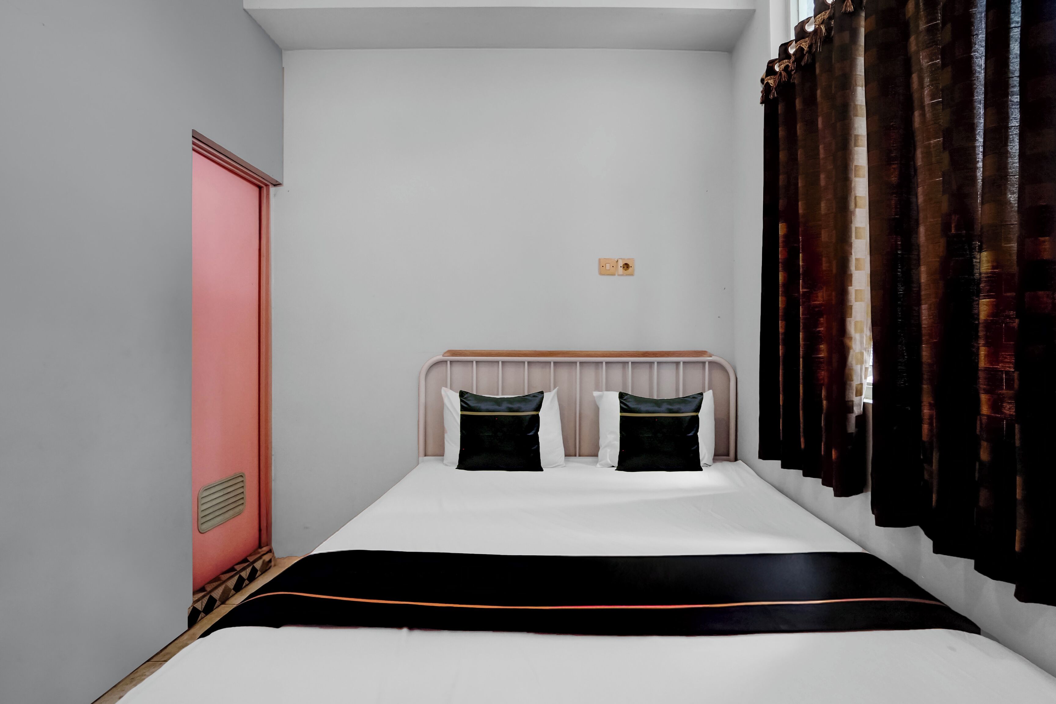 A small, neatly arranged bedroom with a single bed, a wooden headboard, and a window with dark curtains.