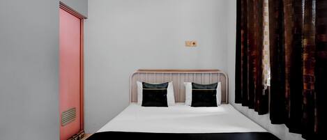 A small, neatly arranged bedroom with a single bed, a wooden headboard, and a window with dark curtains.