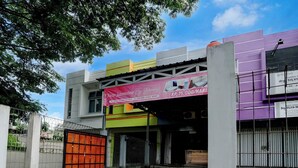 Un edificio con entrada protegida por una reja, un cartel publicitando un nuevo jazmín de Yoreans, y un edificio morado al fondo.