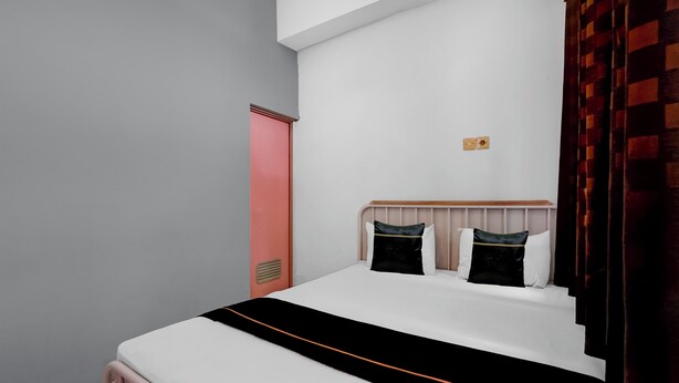 Un dormitorio con cama, cabecera, lámpara de pared y ventana con cortinas.