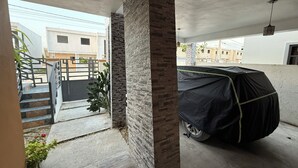 Un'area esterna riparata con un'auto coperta da un telo nero, una scala e un pilastro in mattoni.