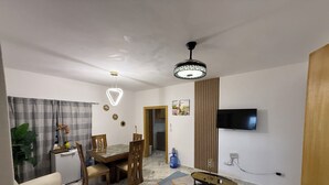 Un soggiorno con divano, tavolo da pranzo e sedie. C'è una TV a muro e una lampada a sospensione.
