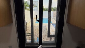 Vista attraverso una finestra con un cancello in metallo, una piscina blu e un’area giochi.
