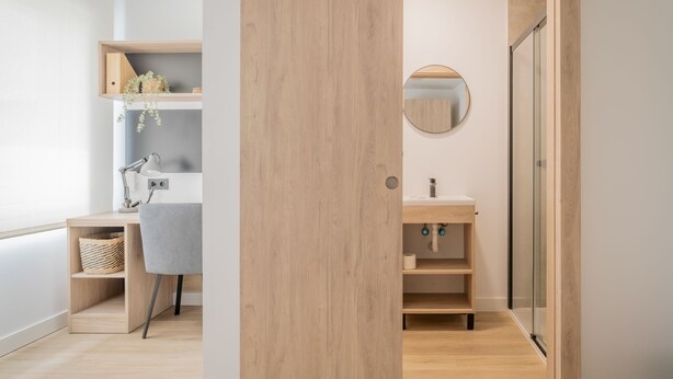 A modern bathroom with a wooden door, a round mirror, and a glass shower enclosure. - Micampus Foronda 7 (Madrid)