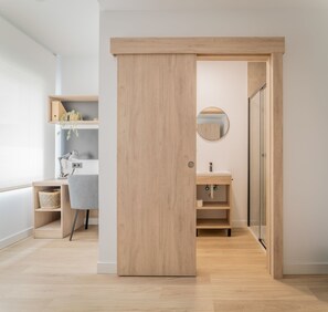 Un baño moderno con puerta de madera, un espejo redondo y mampara de ducha de vidrio.