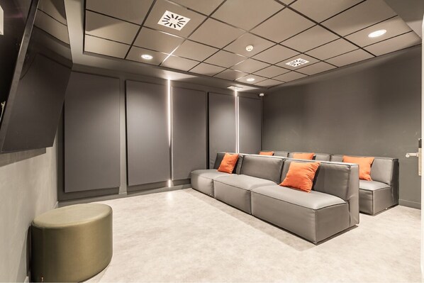 Uma área de espera moderna com sofá e apoio para os pés, televisão de tela plana e teto com iluminação embutida.