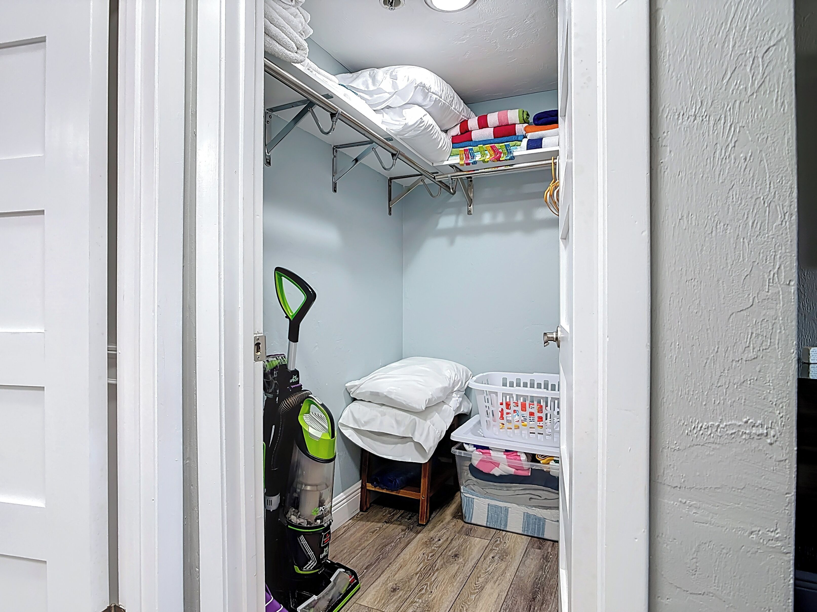 Une petite pièce comprenant un lit superposé, un aspirateur, un panier à linge et une petite table avec un coussin.