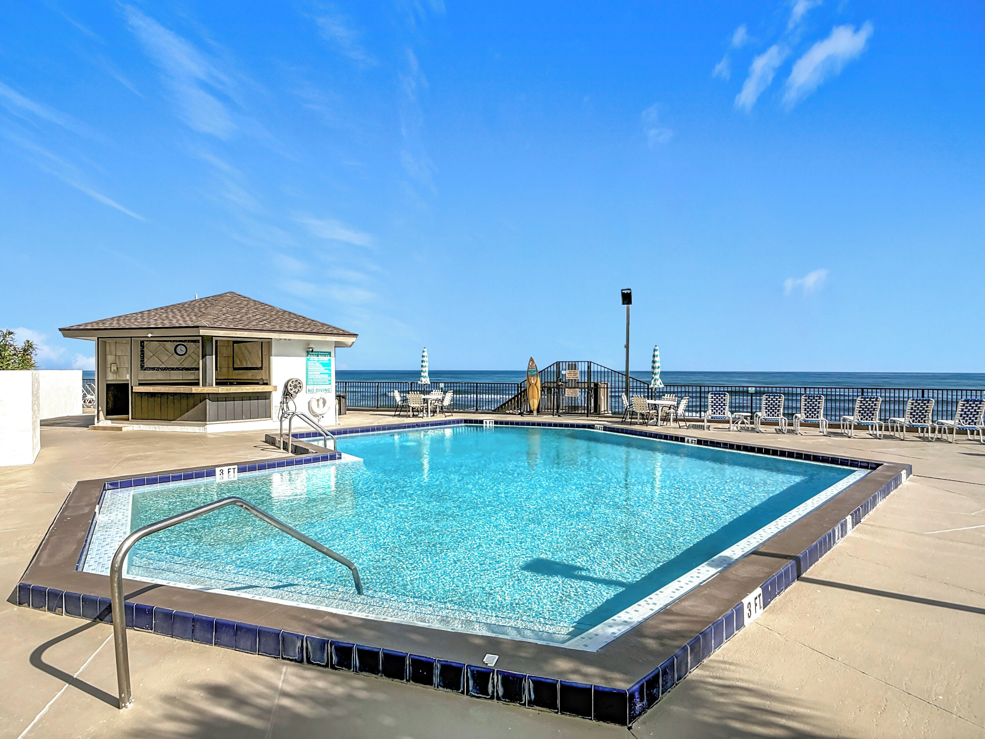 A swimming pool with a lifeguard station, lounge chairs, and a view of the ocean.