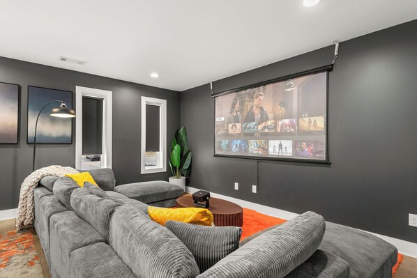 Uma sala de estar moderna com um sofá modular cinza, uma mesa de centro e uma grande tela para assistir.