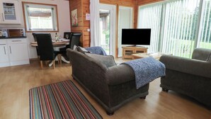 A cozy living room with a wooden interior, a dining area with a table and chairs, a television on a stand, and a kitchen with cabinets and a microwave.