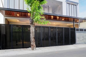 A modern building with a black metal fence, a tree in front, and a clear sky.