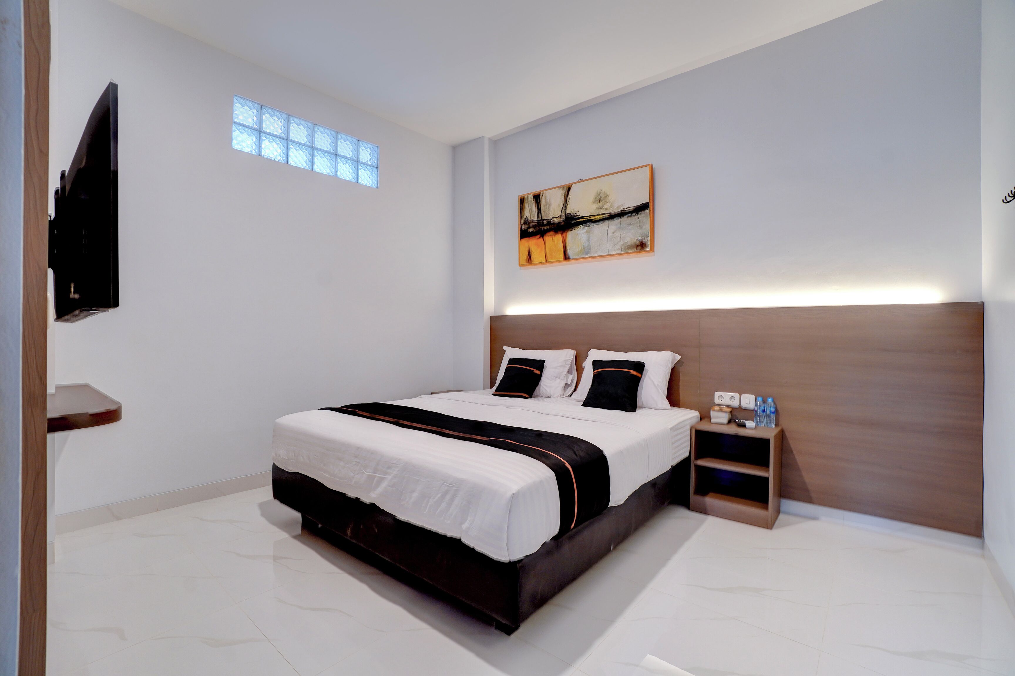 A modern bedroom with a large bed, a nightstand, a TV mounted on the wall, and a window with a view.