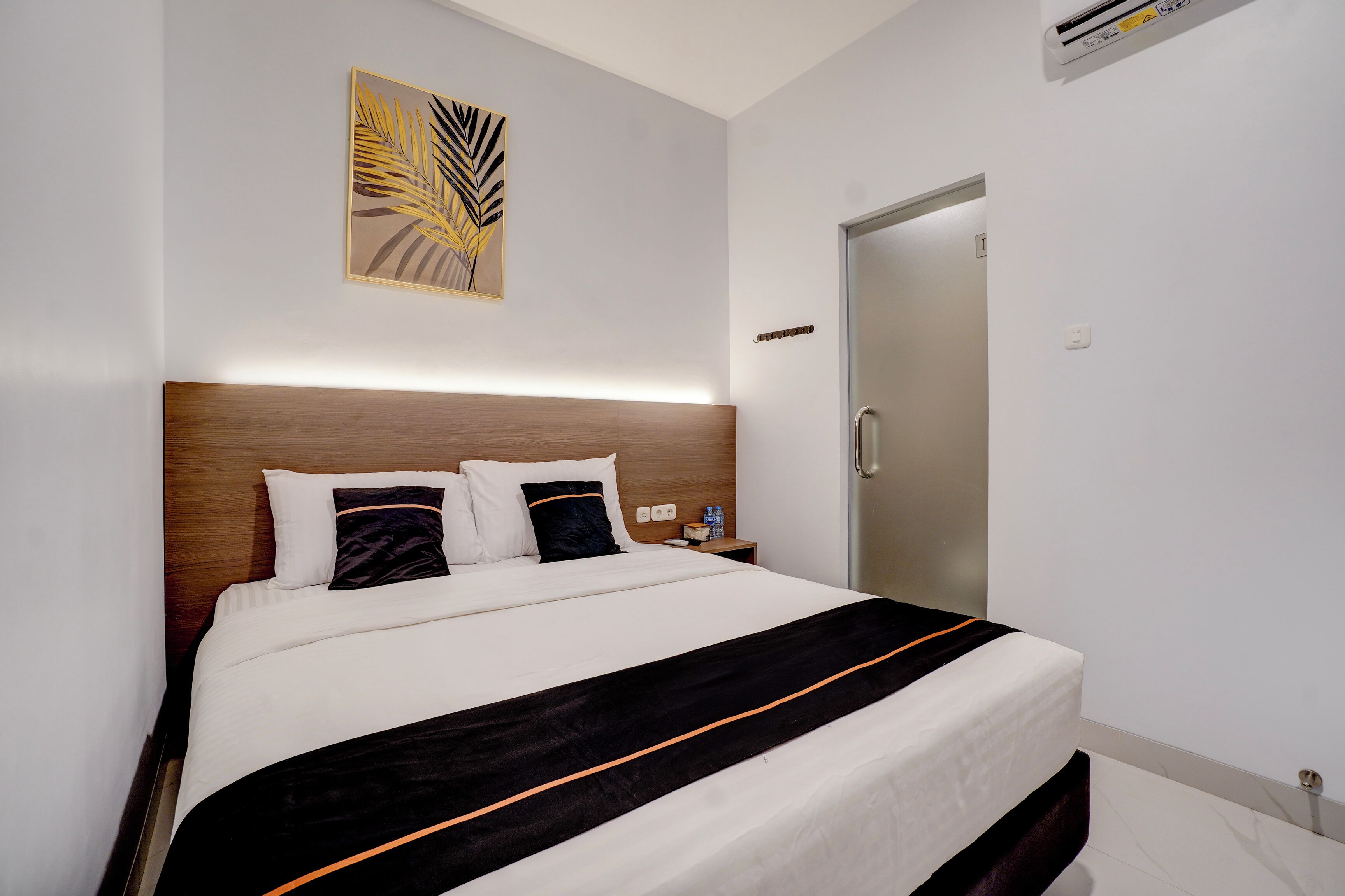 Una cama bien hecha con cabecera de madera, ropa de cama blanca y una manta a rayas negra y naranja.