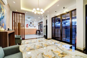 Een moderne hotel lobby met een marmeren vloer, een receptiebalie, een zithoek en grote schuifdeuren die uitkomen op een balkon.