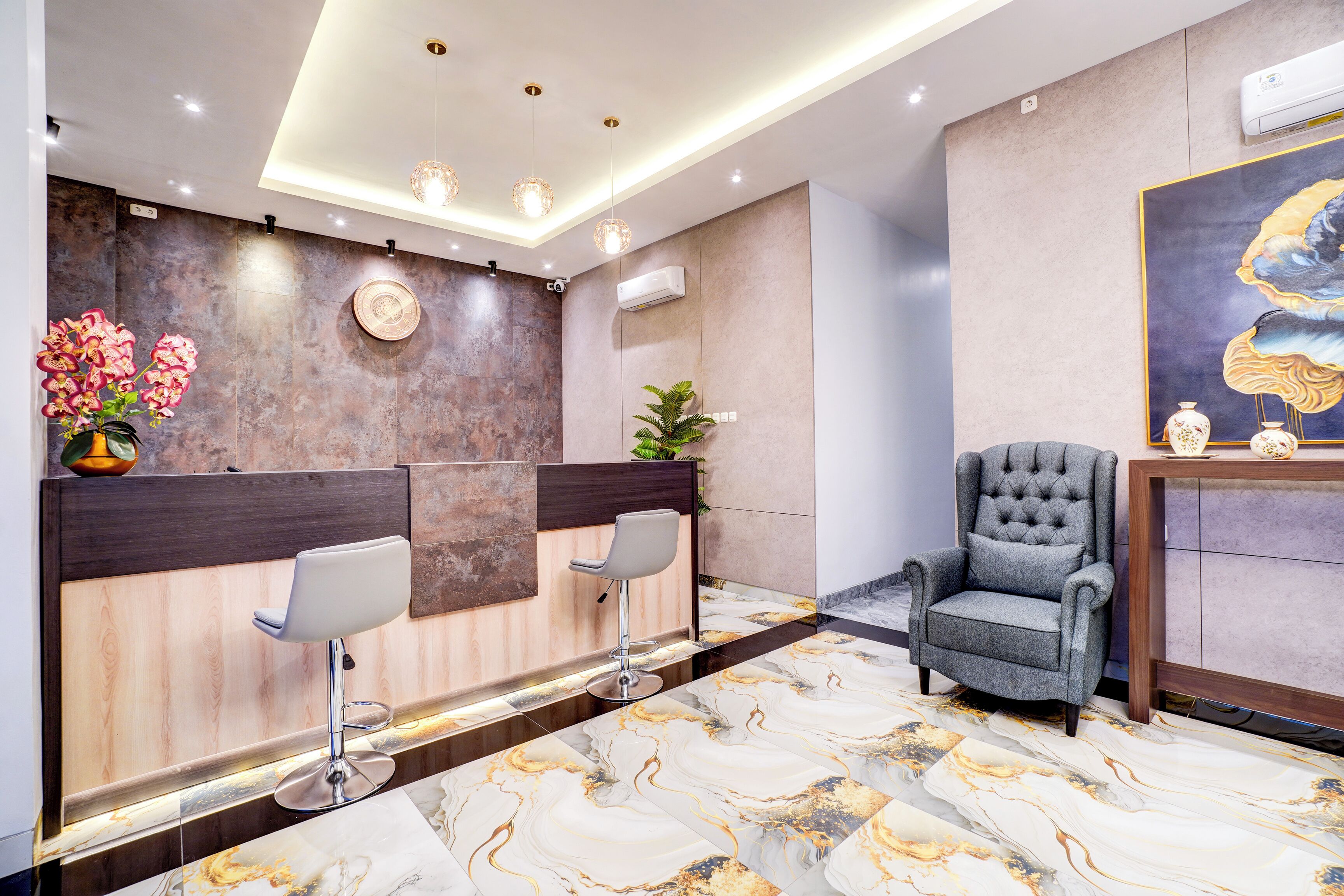 A modern reception area with marble flooring, two bar stools, a grey armchair, and a decorative wall piece.