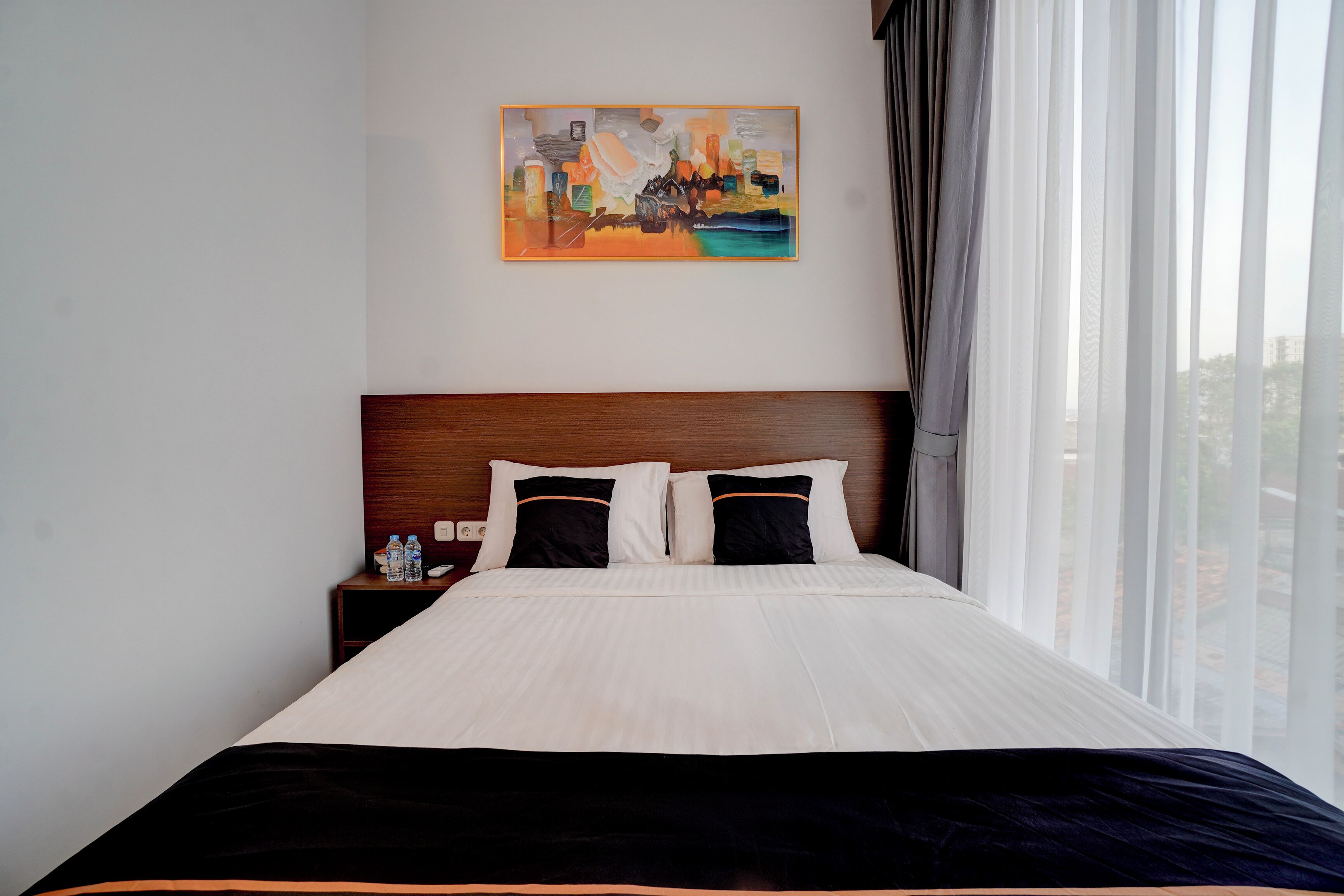 A hotel room with a large bed, a nightstand with a water bottle, and a painting on the wall.