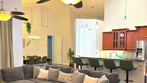 Una sala de estar moderna con un sofá modular, un comedor con sillas, una cocina con armarios de madera y un ventilador de techo.