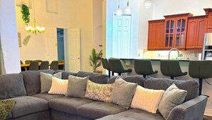 Una sala moderna con un sofá modular, una alfombra estampada, piso de madera y una cocina al fondo.