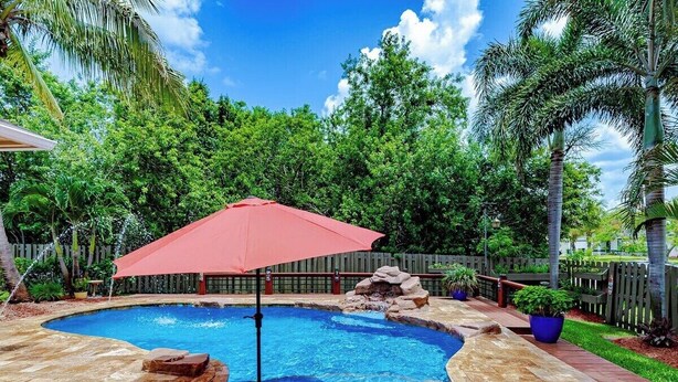 Una piscina con una sombrilla roja, rodeada por una terraza de madera y abundante vegetación.