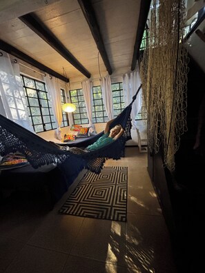A room with a hammock, a bed, a patterned rug, and a window with curtains.