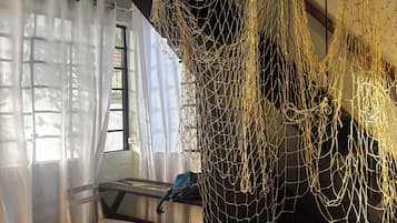 Une pièce avec un plafond en bois, un mur noir et une fenêtre ornée de rideaux légers. On y trouve une chaise et une table sur laquelle est posé un sac bleu.