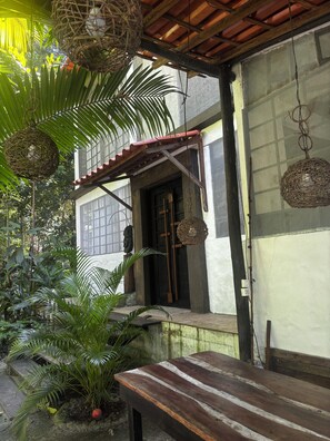A wooden bench, a woven hanging light fixture, and a doorway with a cross.
