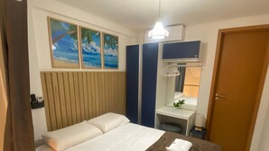 Hotellihuone, jossa on sänky, yöpöytä, peili ja ovi.