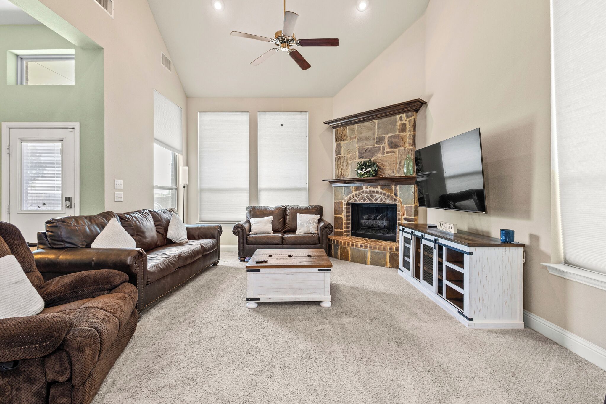 A living room with a fireplace, a television mounted on the wall, and a ceiling fan.