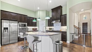 Una cocina amplia con alacenas de madera oscura, electrodomésticos de acero inoxidable y una isla central con taburetes de bar.
