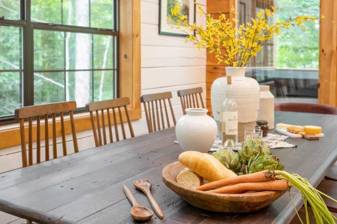 Una mesa de madera con un cuenco de verduras, un florero con flores amarillas y una botella de leche.