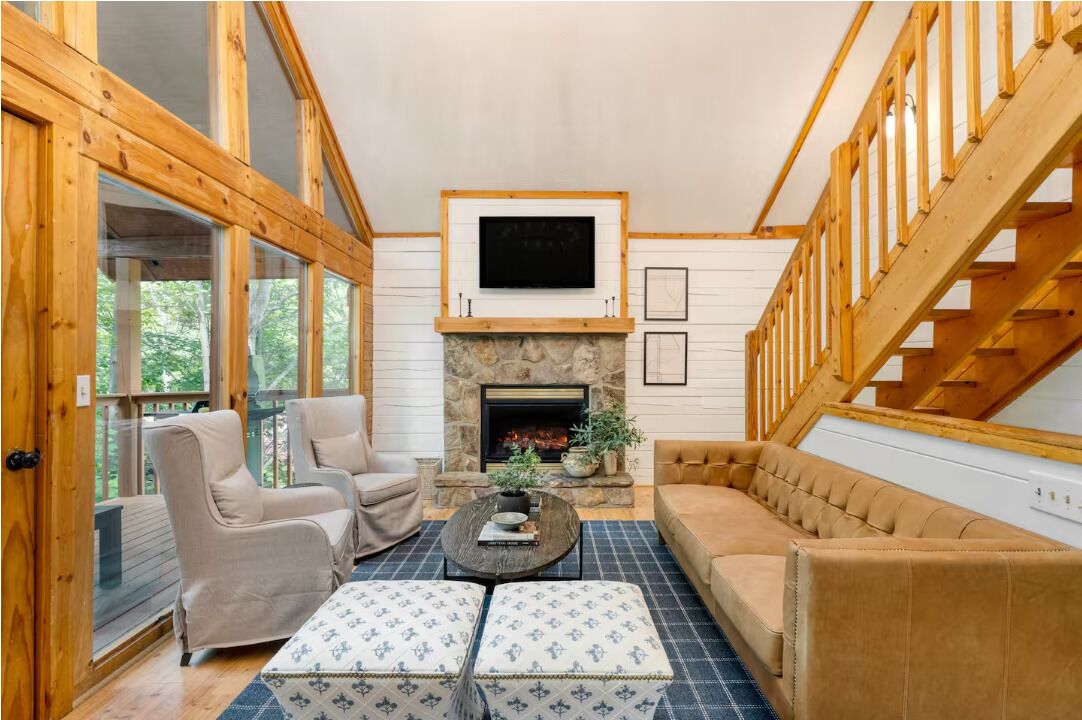 A cozy living room with a stone fireplace, wooden beams, and a large window.