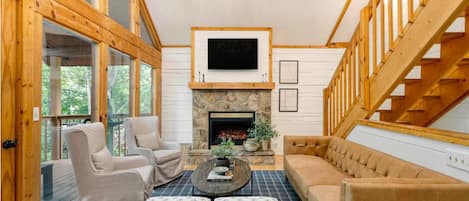 A cozy living room with a stone fireplace, wooden beams, and a large window.