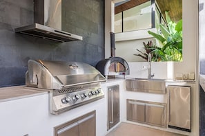 A modern kitchen with a built-in grill, stainless steel cabinets, and a window overlooking greenery. - Private Luxury Villa in Nosara. (Playa Pelada)