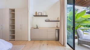Ett modernt kök med öppna hyllor, en inbyggd diskmaskin och utsikt över en frodig trädgård genom en glasdörr.