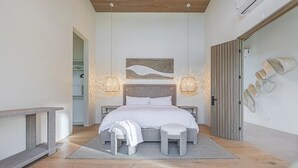 Ett modernt sovrum med en stor säng, två sänglampor, en bänk och en skohylla som är monterad på väggen.
