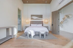 Ein modernes Schlafzimmer mit einem großen Bett, zwei Nachttischlampen, einer Bank und einem an der Wand befestigten Schuhregal.
