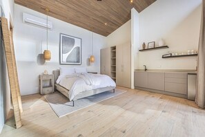 A modern bedroom with a bed, bedside tables, a large abstract painting, and a kitchen area with cabinets and shelves. - Private Luxury Villa in Nosara. (Playa Pelada)