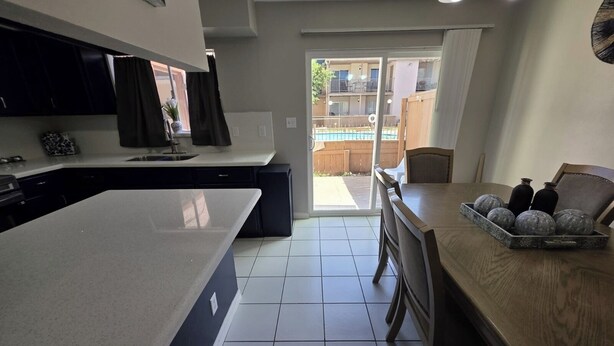A modern kitchen with a large island, a dining area with a wooden table and chairs, and a view of a swimming pool through a sliding glass door. - The Rancho Viejo Getaway (Rancho Viejo)