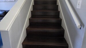 A staircase with dark wooden steps and white handrails, leading to a landing with a white wall and a light switch. - The Rancho Viejo Getaway (Rancho Viejo)
