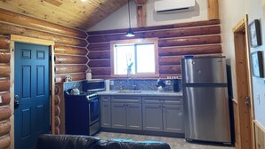 L’intérieur d’une cabane en rondins comprend un espace cuisine équipé d’une cuisinière, d’un four à micro-ondes et d’un réfrigérateur.