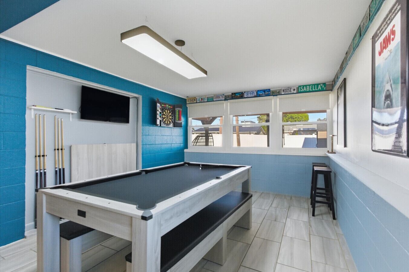 Ein Billardtisch in einem Raum mit blauen Wänden, einer Dartscheibe und einem an der Wand befestigten Fernseher.