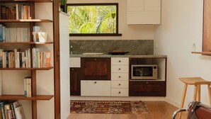 Un salon moderne avec un canapé en cuir marron, une bibliothèque en bois et un coin cuisine équipé d’un four à micro-ondes.