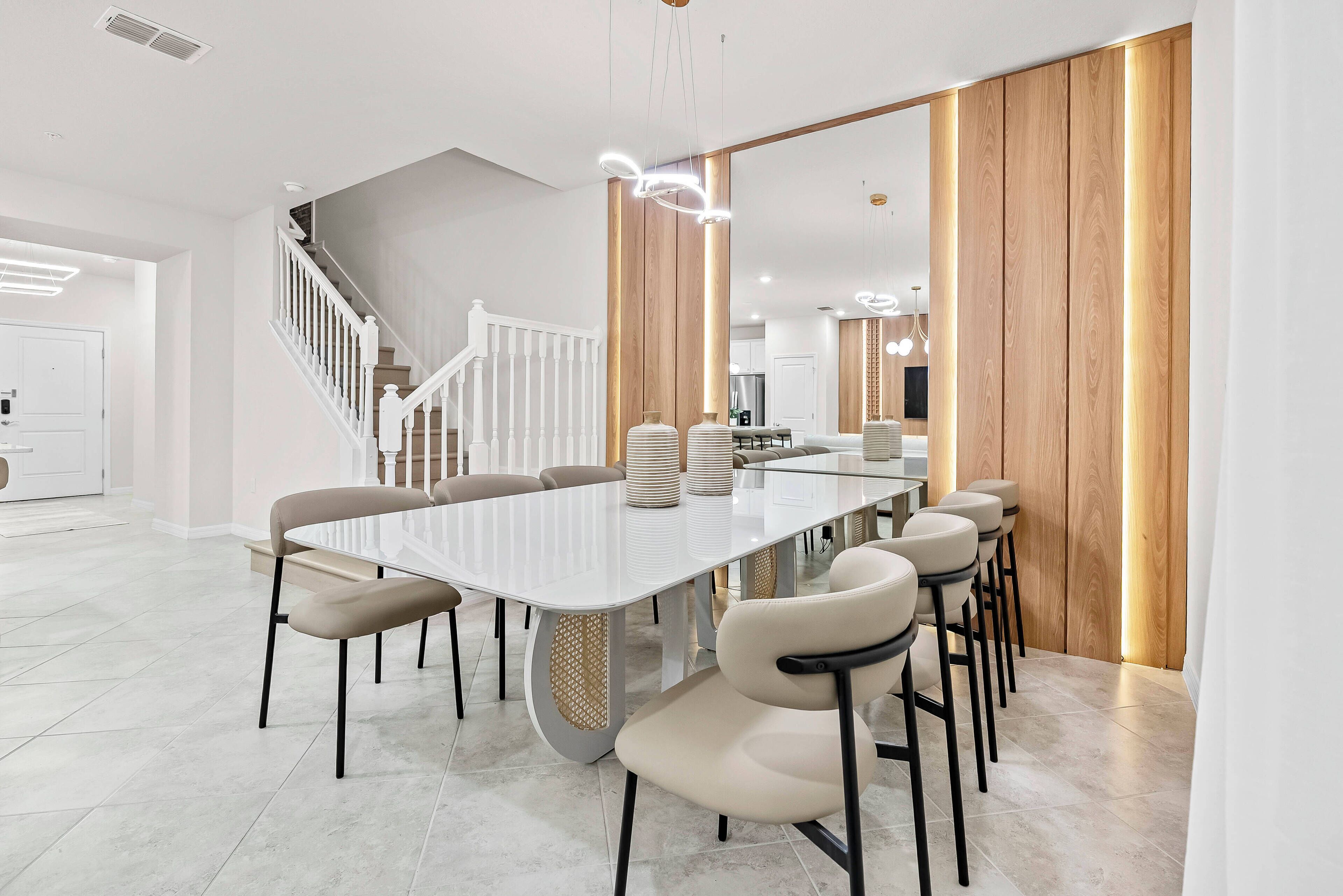 A modern dining area with a long white table, beige chairs, and a wooden accent wall.